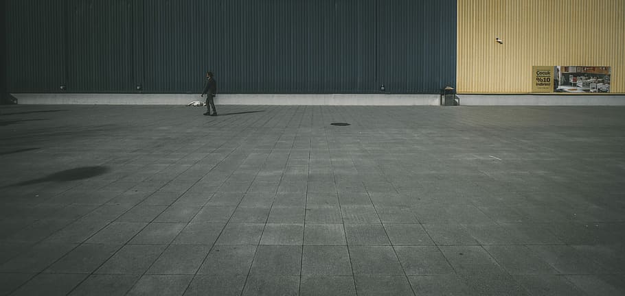 person walking on concrete pavement, person standing on gray concrete flooring near building during daytime HD wallpaper