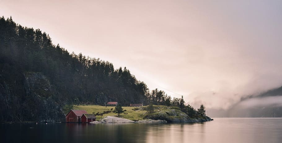 green mountain beside sea under gray sky, leafed trees near body of water HD wallpaper