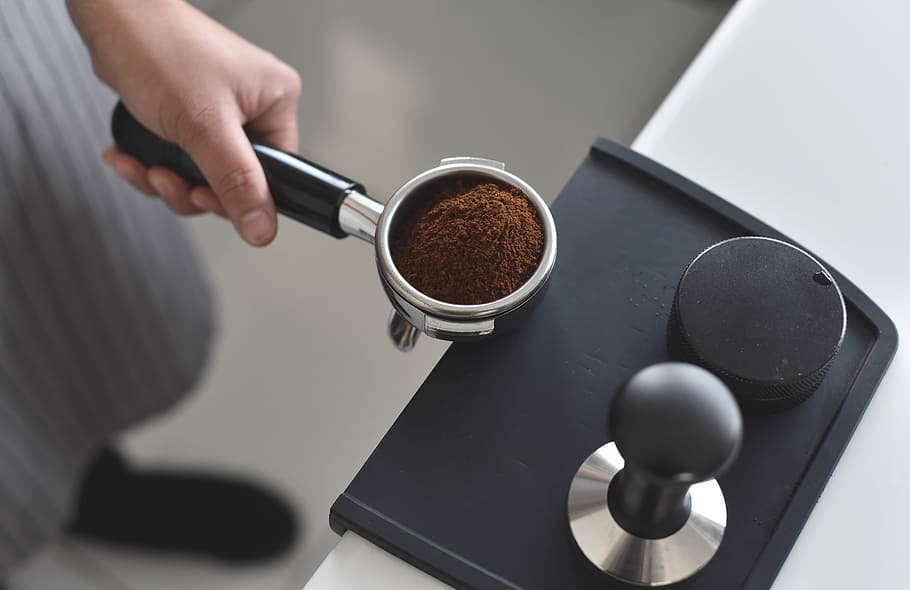 person holding pot with coffee powder, black coffeemaker accessory