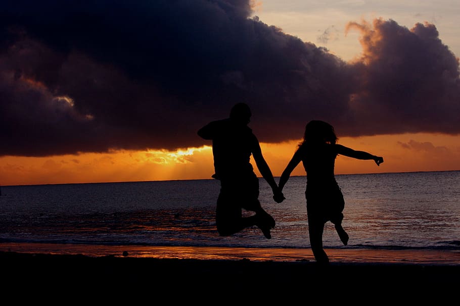 silhouette photo of two person's jumping in front of body of water HD wallpaper