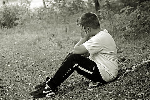 grayscale photo of man holding face while sitting on grass field HD wallpaper