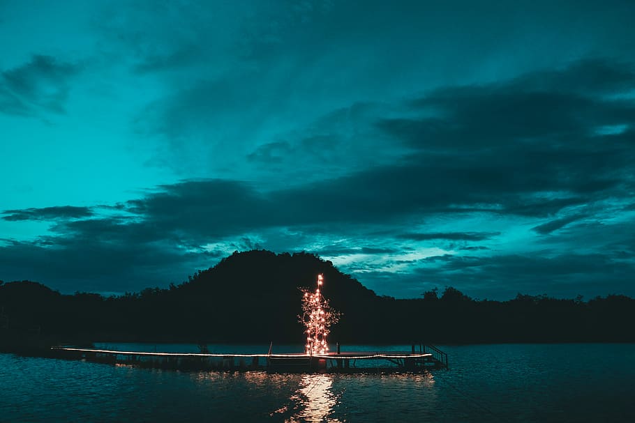 lighted tree decor on wooden dock, light on dock near ocean and mountain during night time HD wallpaper