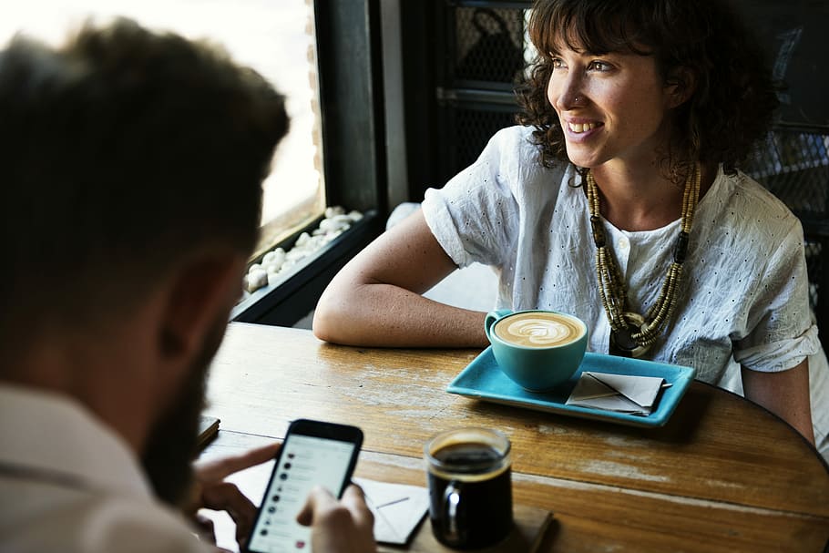 man using phone sitting in front of woman, meeting, date, smiling