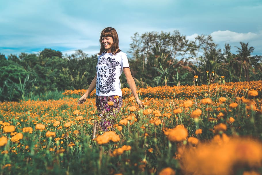 Happy young woman on a marigold field. Bali island, photo of woman in white crew-neck T-shirt walking on flower field during daytime, HD wallpaper