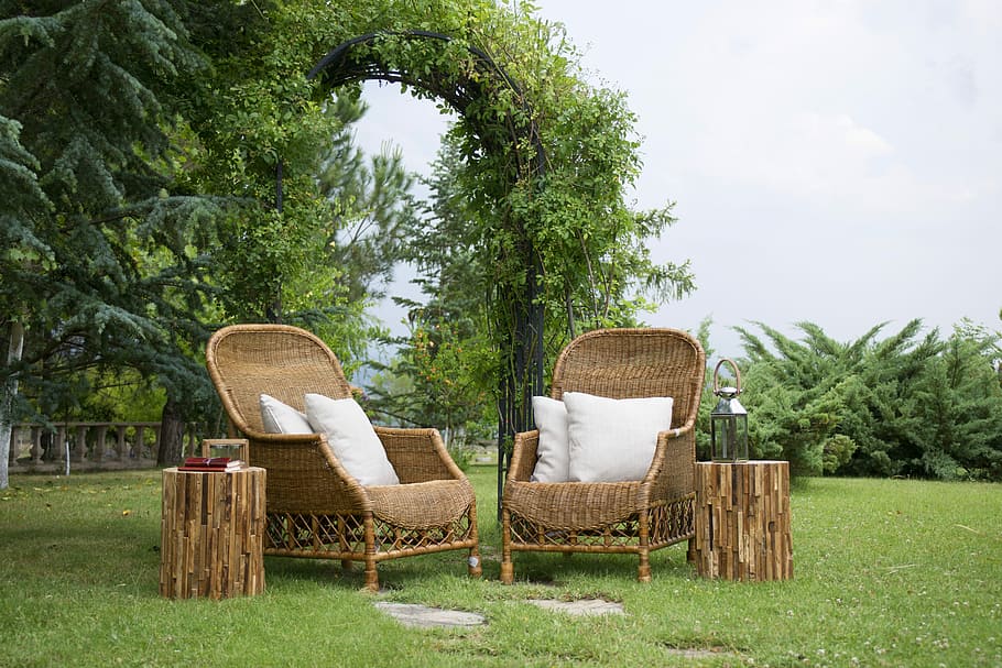 two brown wicker armchairs with white throw pillows beside two round tables on grass field, HD wallpaper