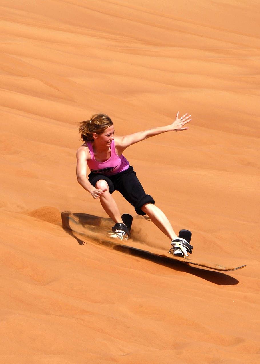 woman in pink tank top and black pants sand skiing, sandboarding