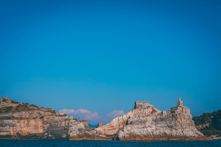 castle on mountain cliff near tree, body of water under blue sky HD wallpaper