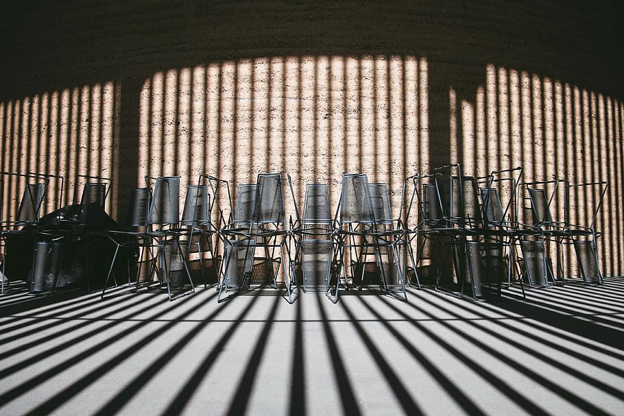 Stacked chairs along the wall covered by shadows of the building, gray metal framed chair lot inside room at daytime HD wallpaper