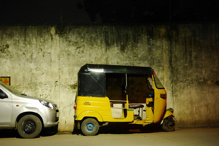 auto rickshaw beside concrete wall and silver car, yellow and black auto rickshaw parked by gray concrete wall