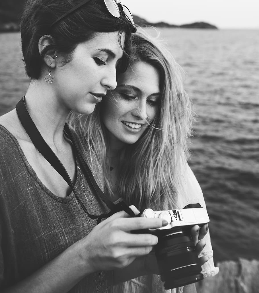 grayscale photo of woman holding camera beside woman, calm, dom