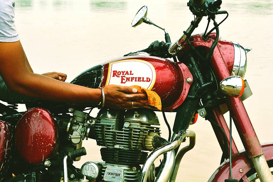 person wiping red and grey Royal Enfield motorcycle, bike, rider