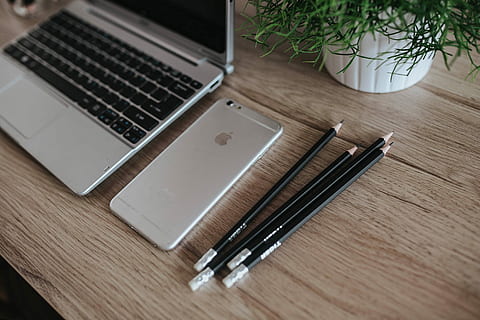 Silver Acer laptop on a wooden desk with a green plant, pencils and an Apple iPhone HD wallpaper