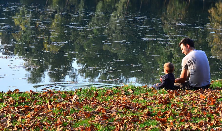 man in gray t-shirt sitting beside boy near body of water, child