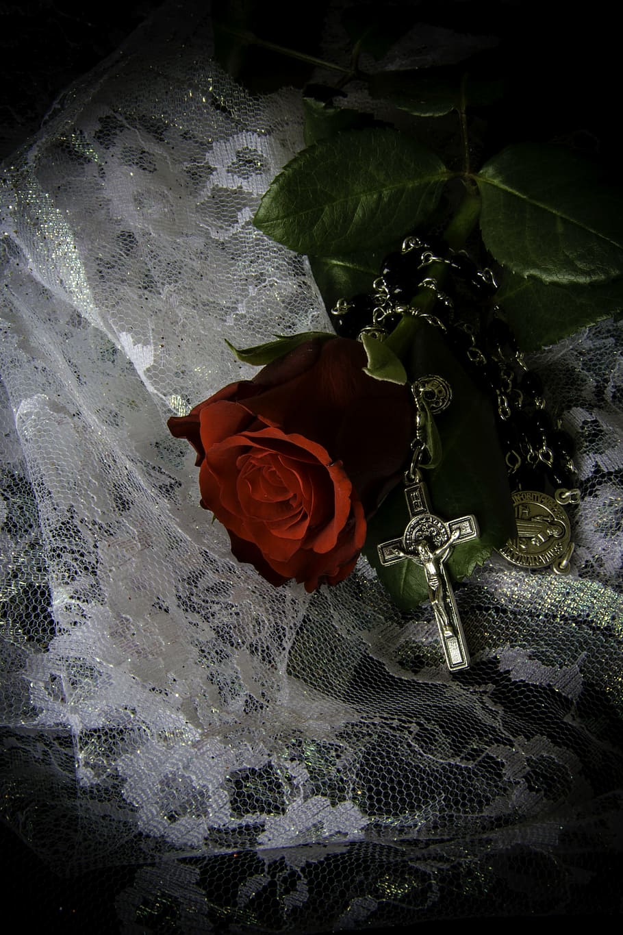 red rose beside silver-colored rosary on white lace textile, crucifix