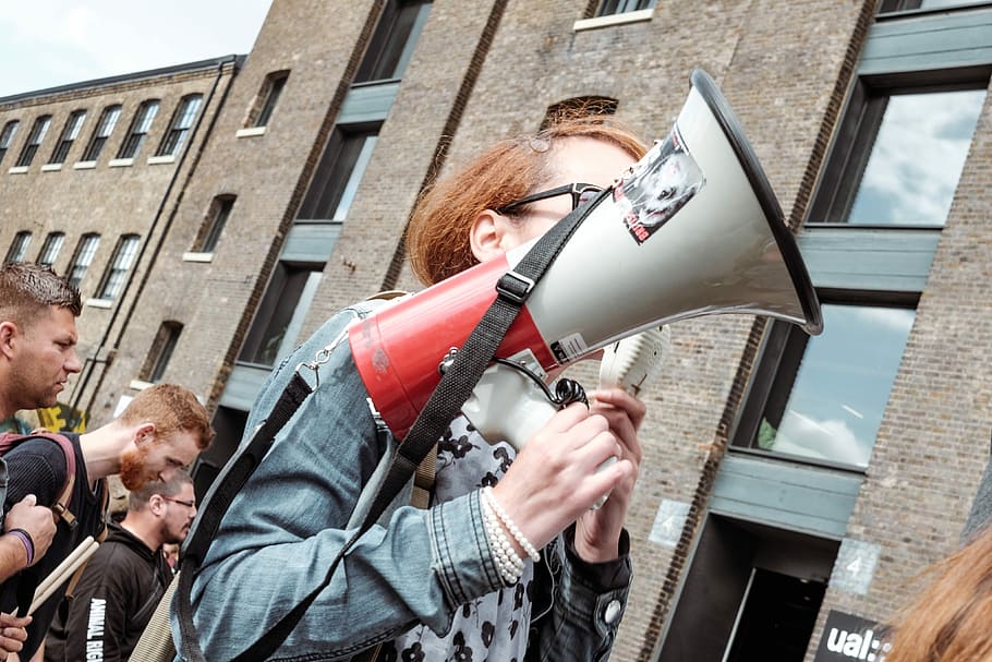 woman holding red and white megaphone standing near building, woman speaker thru megaphone, HD wallpaper