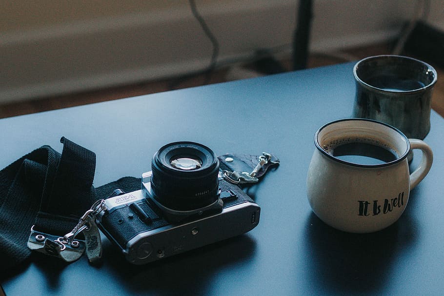 black DSLR camera beside ceramic cup filled with coffee, black and gray film camera laid on gray table HD wallpaper