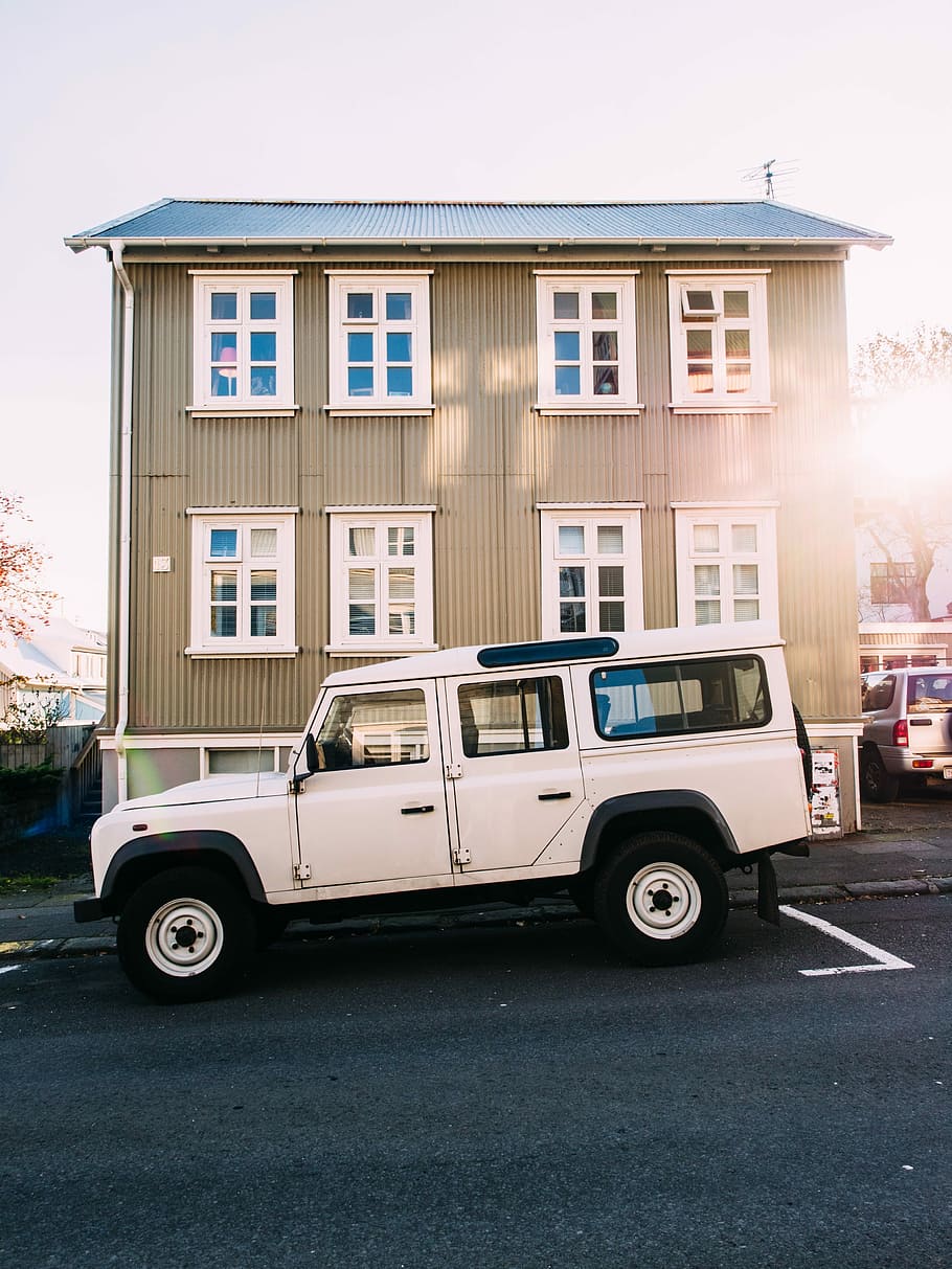 white Land Rover Defender SUV parked in front of brown 3-story building under gray clouds HD wallpaper