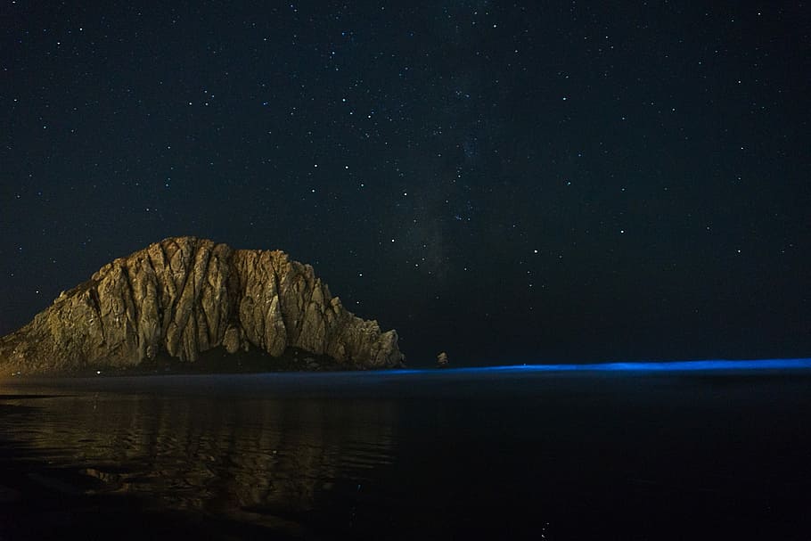 gray rock formation near sea at nighttime, brow rock formation under starry sky HD wallpaper