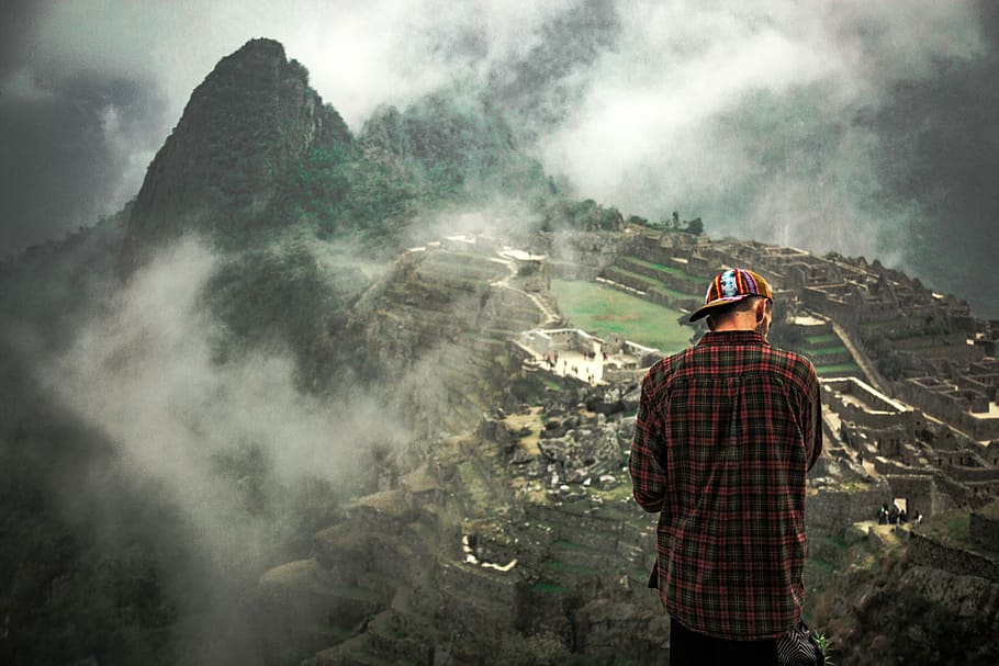 man standing on cliff facing mountain rice terraces, man in red and gray plaid dress shirt and cap standing on top of mountain HD wallpaper