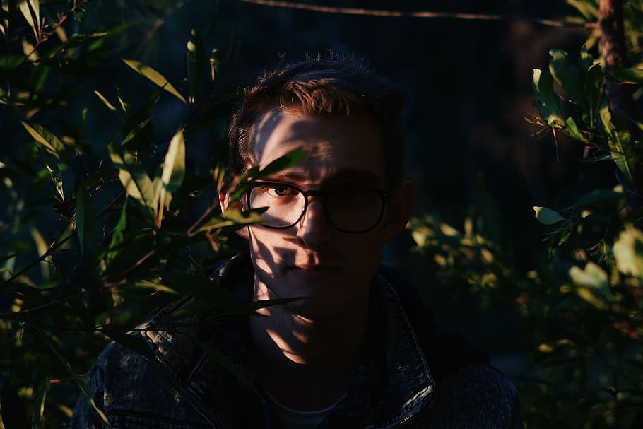 photography of man standing while wearing eyeglasses between near green leaf plants, man standing near green plants HD wallpaper