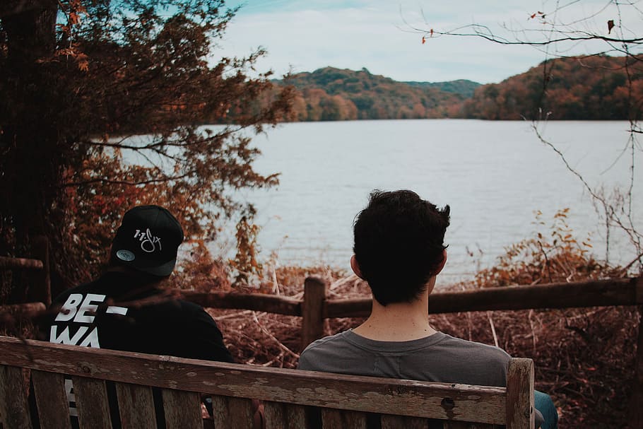 two men sitting on wooden bench looking at body of water, two men sitting on brown wooden bench while staring at lake HD wallpaper