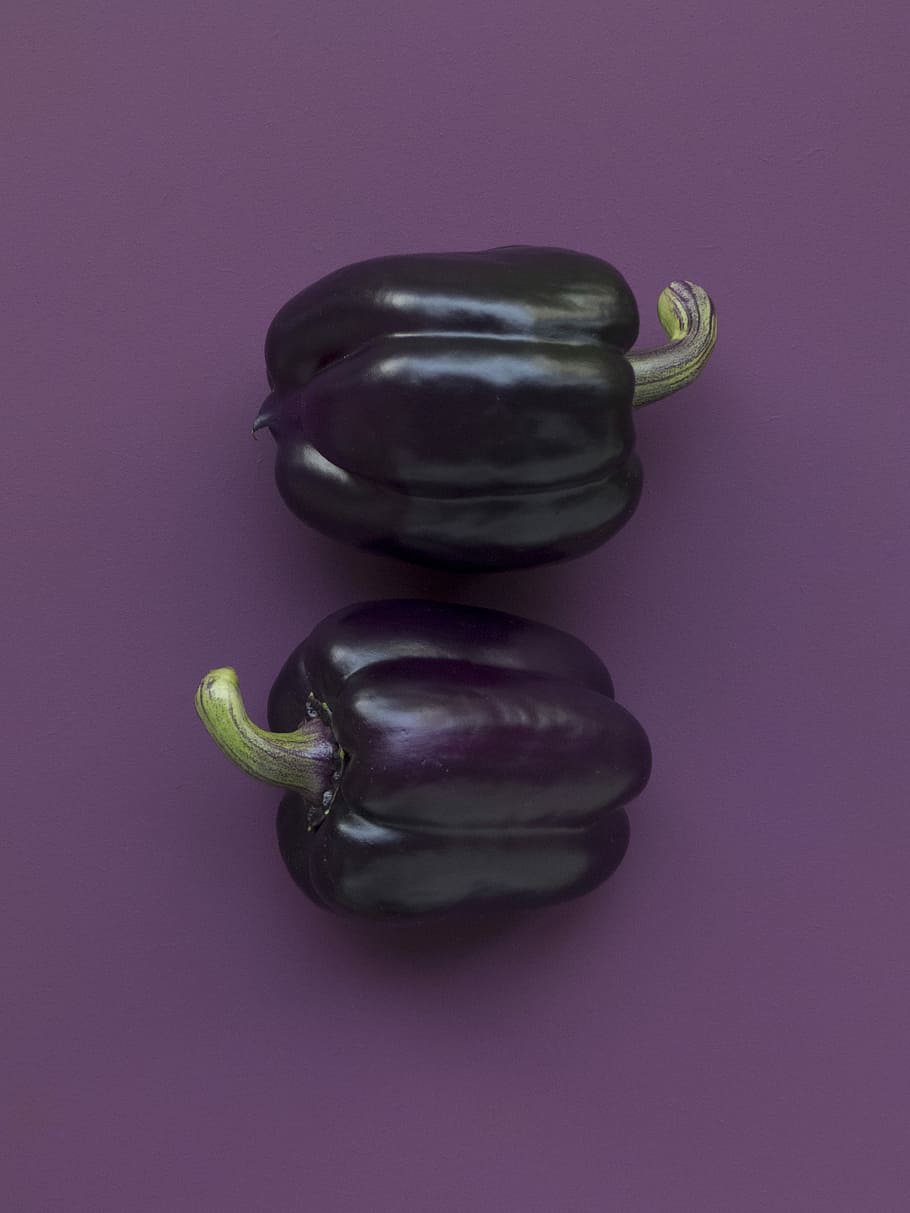 two purple bell peppers on purple surface, two purple bell papers on purple surface