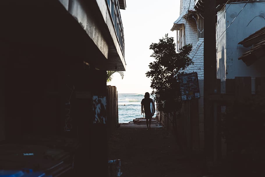 Surfer walking through the alley towards the ocean, silhouette photo of man near body of water HD wallpaper