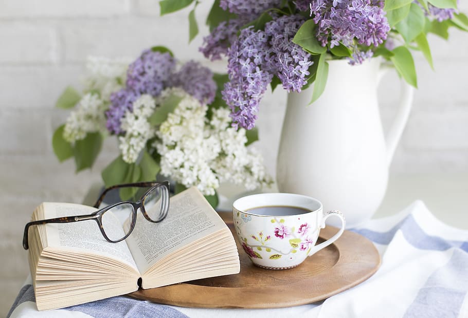 white open book with eyeglasses near teacup, coffee, flowers