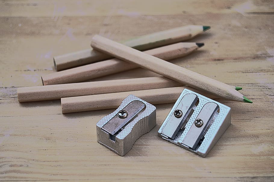 five brown pencils and two silver sharpeners on wooden surface