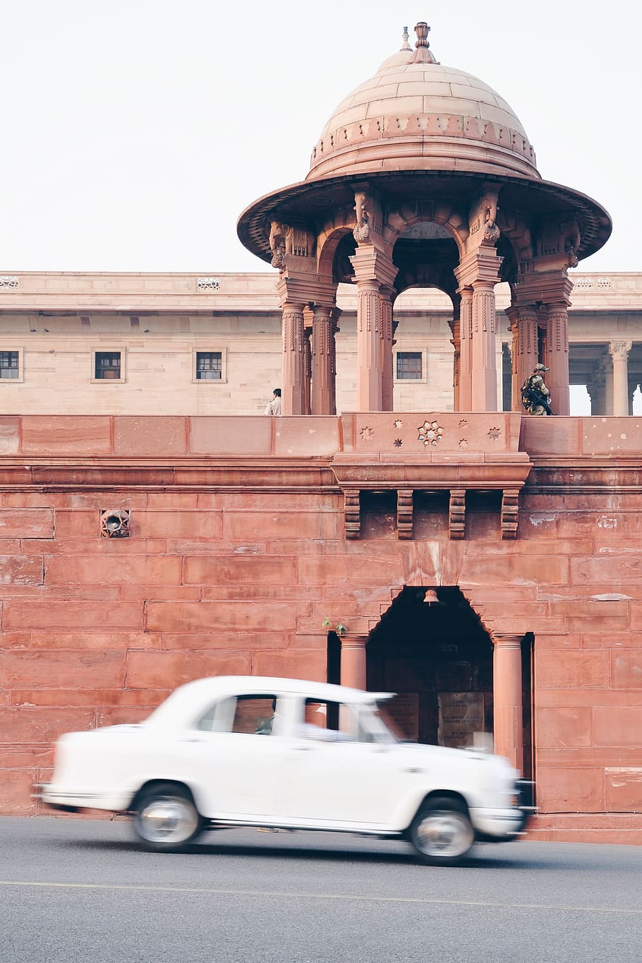 white sedan driving near pink structure, white sedan passing brown architectural structure at daytime HD wallpaper
