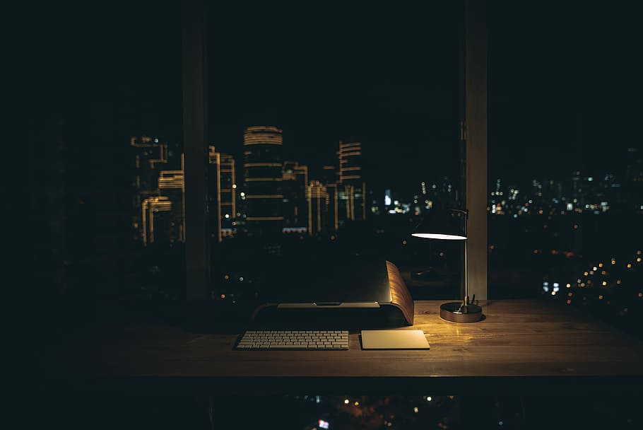 lit desk lamp on top of desk, flat screen monitor, wireless keyboard, and touch pad on wooden surface near window, HD wallpaper