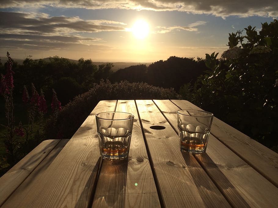 two clear drinking glasses on brown wooden table, sunset, sunrise