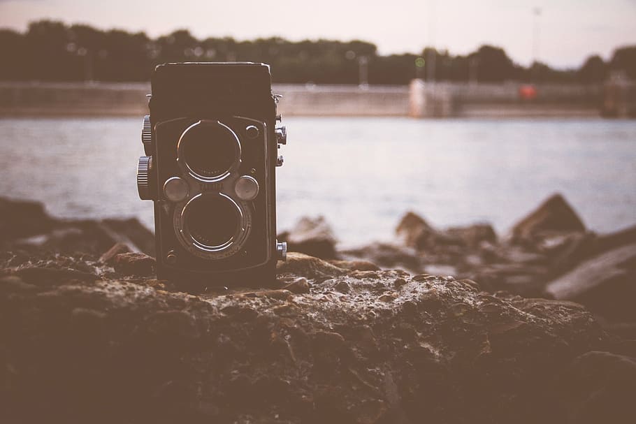 black and grey film camera on brown boulder near body of water