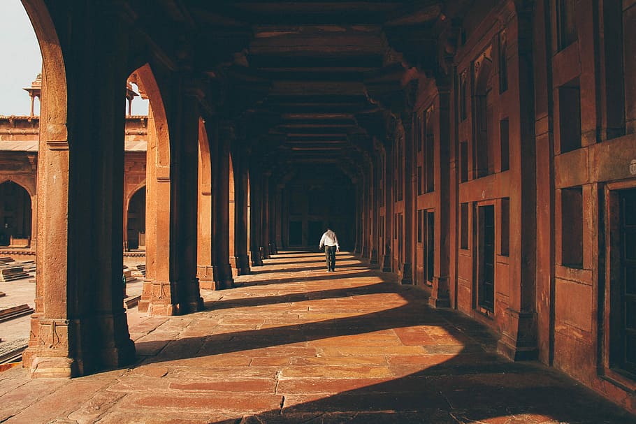 person walking on walkway, person walking on concrete hallway with the reflection of concrete post at daytime HD wallpaper