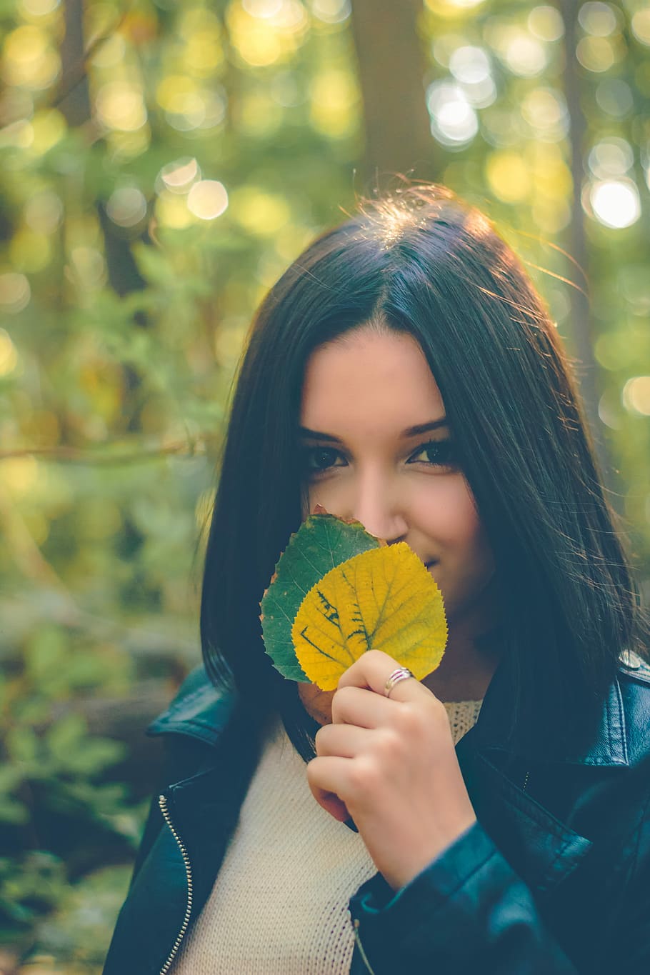 woman holding yellow and green leaves, woman covering her mouth with green and yellow leaves