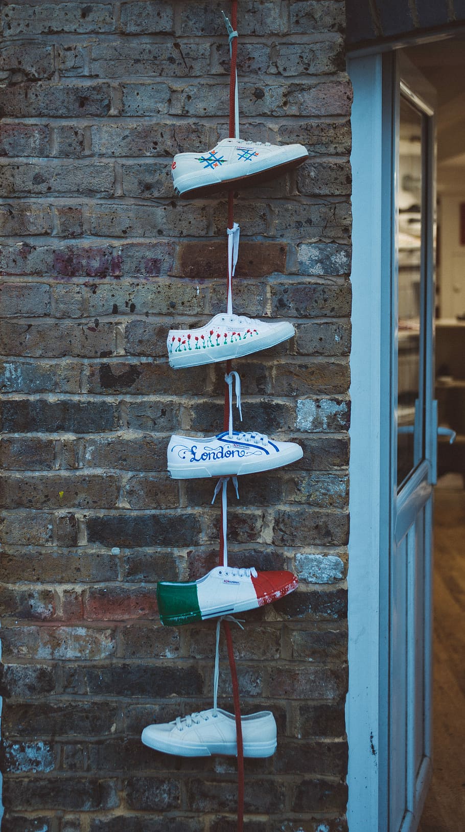 five white sneakers hanged near white door, five unpaired shoe tied up on brick wall