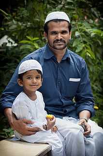 man in blue dress shirt sitting beside toddler in white thobe HD wallpaper