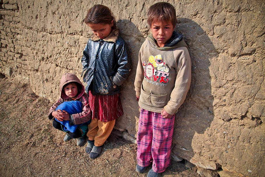 three children leaning on brown concrete wall photo, poor, mud village