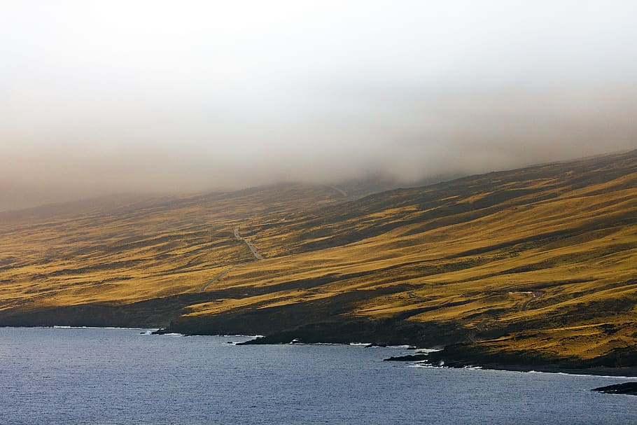 in distant photo of beach and landscape field with fogs, brown and black mountain near body of water HD wallpaper