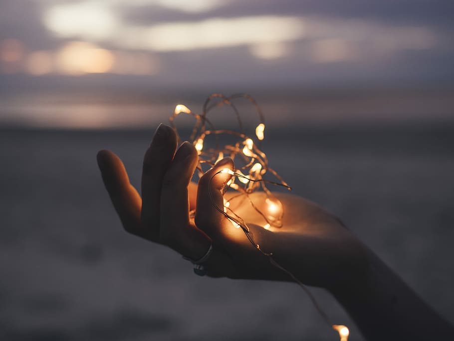 selective focus photography of person holding lighted brown string light, person's right hand holding lighted yellow string lights selective focus photo