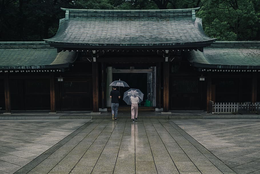 two people holding umbrellas near brown building during rainy season, two person in front of temple