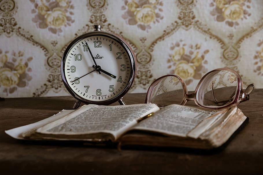 round gray analog desk clock beside eyeglasses and opened book on brown wooden surface HD wallpaper