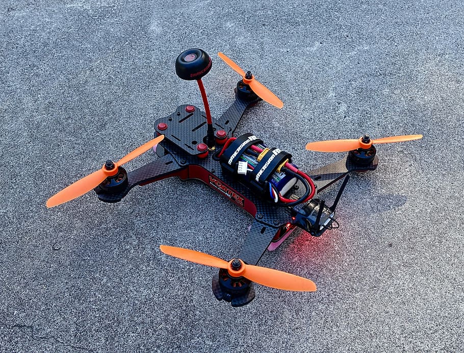 orange and black radio-controlled drone on gray concrete, quadcopter