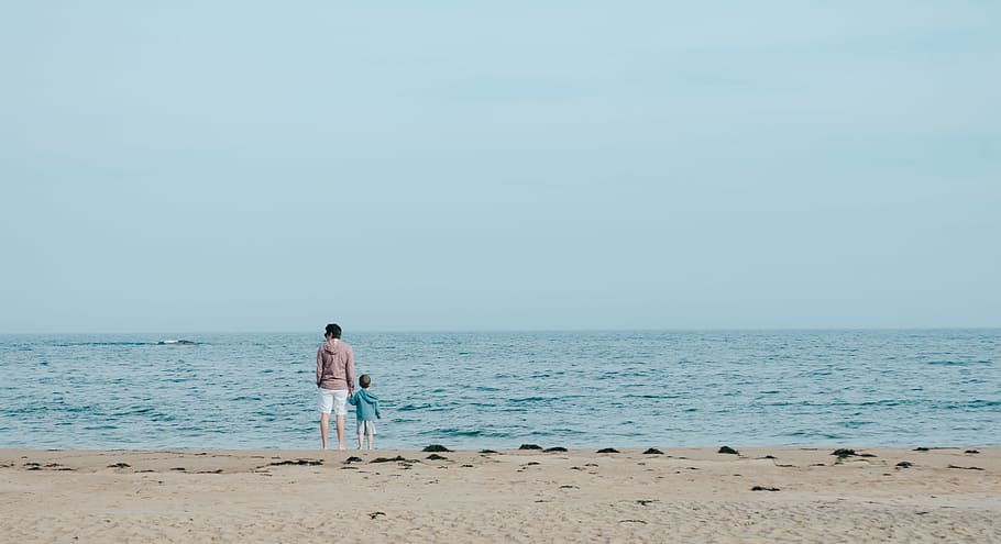 man and toddler standing on shore, person and toddler standing on seashore during daytime HD wallpaper