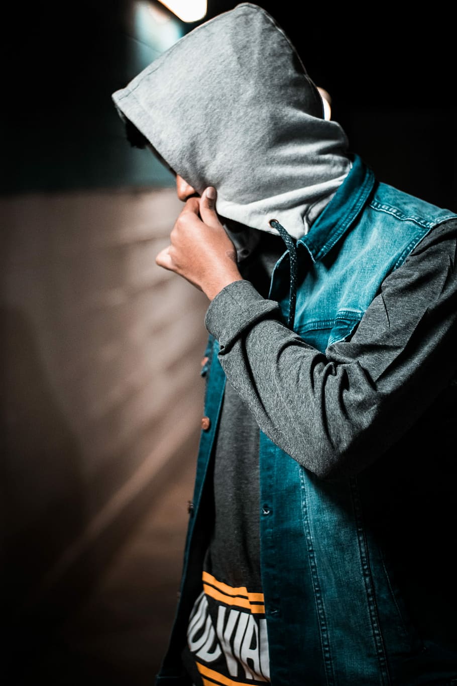man wearing denim jacket standing near wall, person wearing black and blue hoodie