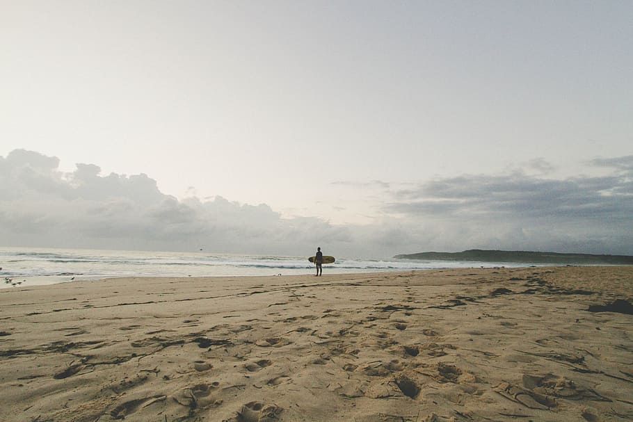 man standing by the seashore with surfboard, man holding surfboard standing on shoreline HD wallpaper