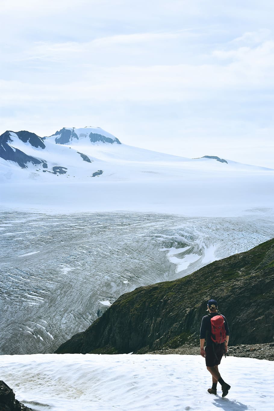 man walking on snow facing mountain, man standing on alp mountain cliff HD wallpaper