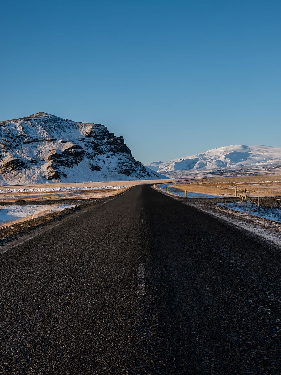 empty concrete road with snow capped mountain background, road way beside body of water and mountain during day time HD wallpaper