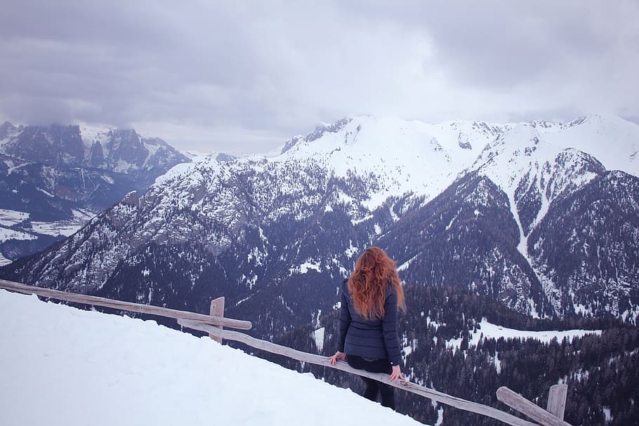 woman sitting on brown fence in front of mountain at daytime HD wallpaper
