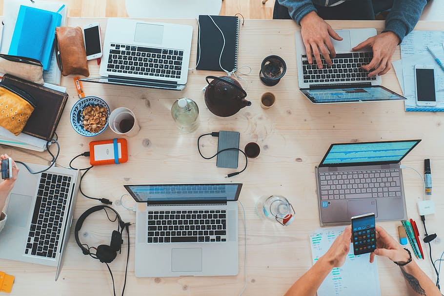 people sitting down near table with assorted laptop computers, gray laptop computers and assorted-type gadgets and items on brown wooden table HD wallpaper